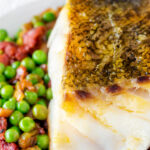 Close up pan fried cod loin with crispy skin, chorizo, peas and leeks.