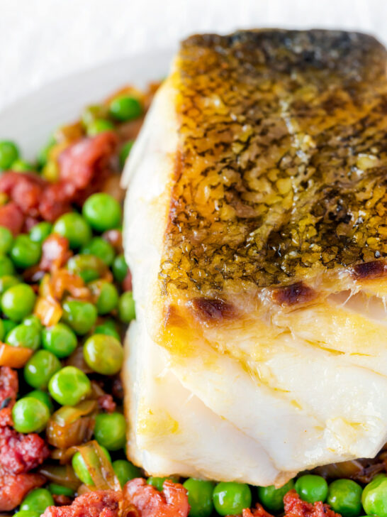 Close up pan fried cod loin with crispy skin, chorizo, peas and leeks.