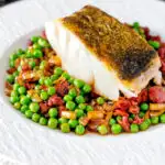 Pan fried cod loin with chorizo sausage, peas and leeks featuring a title overlay.