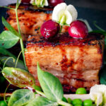 Close up twice cooked pressed crispy pork belly with port cherries and peas.