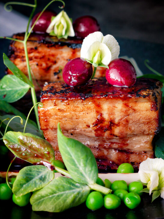 Close up twice cooked pressed crispy pork belly with port cherries and peas.