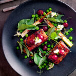 Overhead twice cooked pressed crispy pork belly with port cherries and peas.