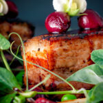 Close up pressed crispy pork belly with port cherries and peas.