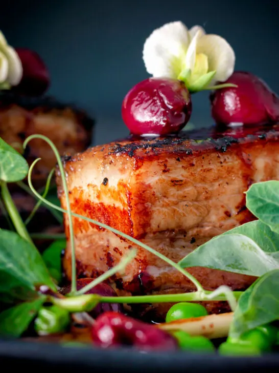 Close up pressed crispy pork belly with port cherries and peas.