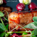 Close up pressed crispy pork belly with port cherries and peas featuring a title overlay.