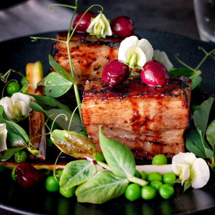 Twice cooked pressed crispy pork belly with port cherries peas and pea shoots.