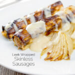 Homemade skinless sausages wrapped in charred leeks with pear and cider sauce featuring a title overlay.