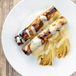 Overhead skinless sausages wrapped in charred leeks with pear and cider sauce.