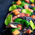 Bacon pasta with squid ink spaghetti, spinach and tomatoes.
