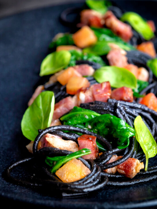 Bacon pasta with squid ink spaghetti, spinach and tomatoes.