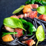 Close up bacon pasta with squid ink spaghetti, spinach and tomatoes.