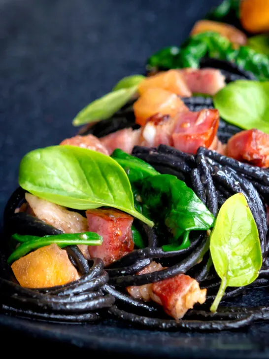 Close up bacon pasta with squid ink spaghetti, spinach and tomatoes.