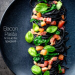 Overhead bacon pasta with squid ink spaghetti, spinach and tomatoes.