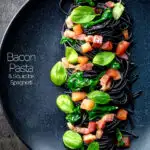 Overhead bacon pasta with squid ink spaghetti, spinach and tomatoes.