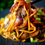 Beef noodle stir fry with sweet chilli sauce and red peppers being eaten with chopsticks.