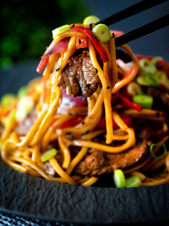 Beef noodle stir fry with sweet chilli sauce and red peppers being eaten with chopsticks.