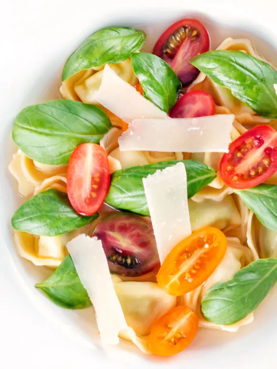 Overhead close up tomato consomme or brodo with tortellini and cherry tomatoes.