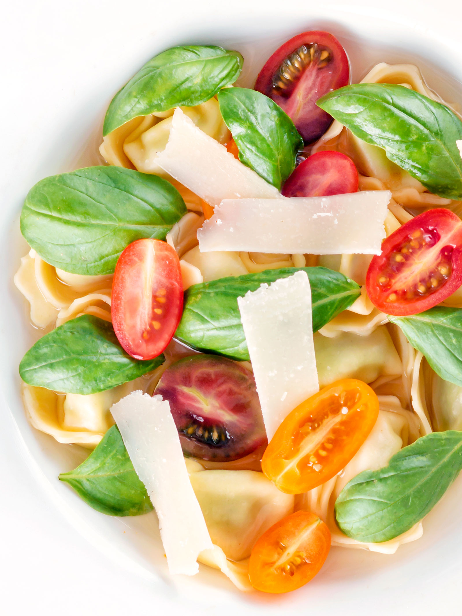 Overhead close up tomato consomme or brodo with tortellini and cherry tomatoes.