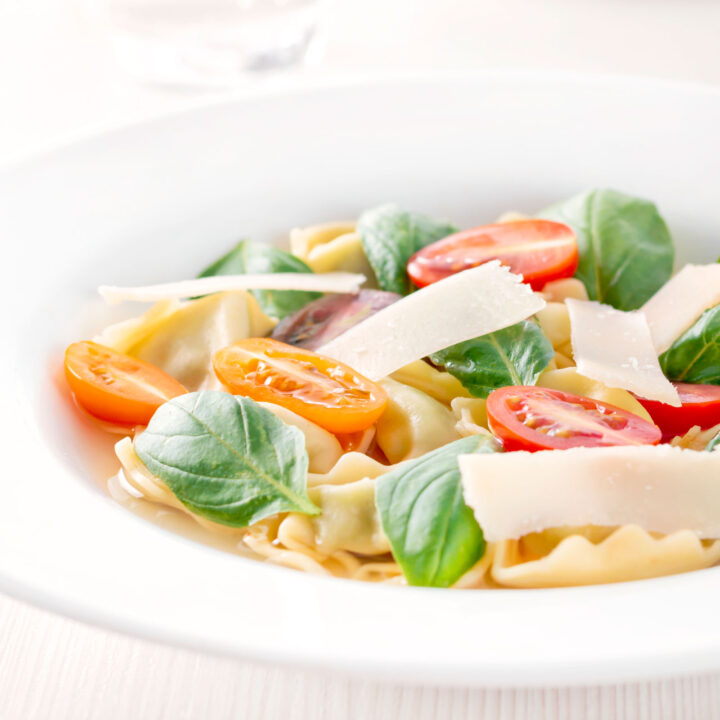 Tomato consomme or brodo with tortellini, cherry tomatoes, and fresh basil.