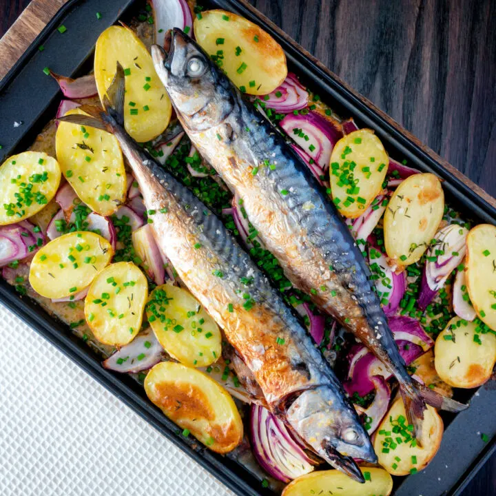 Baked whole mackerel with salad potatoes, red onions and chives on a baking tray.