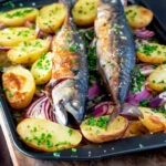 Baked whole mackerel with salad potatoes, red onions on a baking tray.