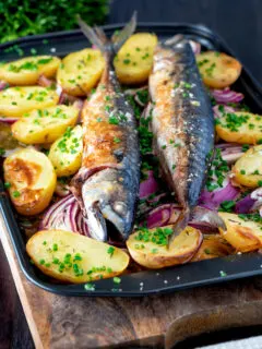 Baked whole mackerel with salad potatoes, red onions on a baking tray.
