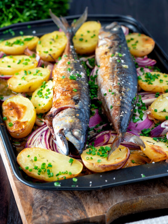 Baked whole mackerel with salad potatoes, red onions on a baking tray.