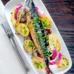 Overhead baked whole mackerel with salad potatoes, red onions and chives.