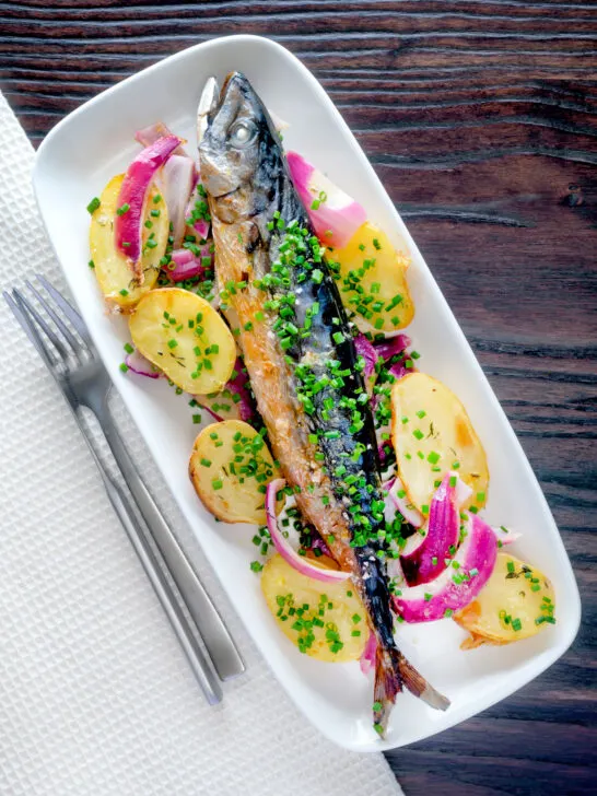 Overhead baked whole mackerel with salad potatoes, red onions and chives.