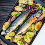 Overhead baked whole mackerel with salad potatoes, red onions on a baking tray.