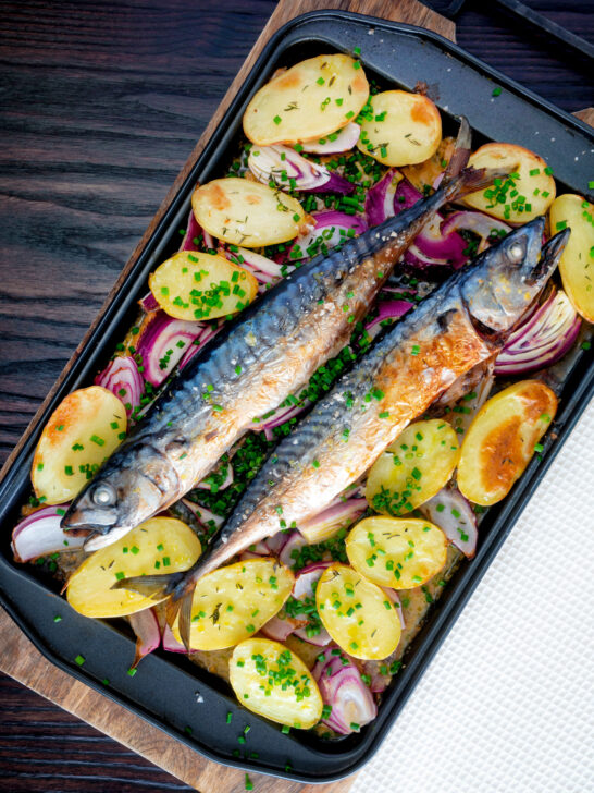 Overhead baked whole mackerel with salad potatoes, red onions on a baking tray.