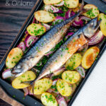 Overhead baked whole mackerel with salad potatoes, red onions on a baking tray featuring a title overlay.