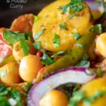 Close up chana aloo, an Indian chickpea and potato curry served with red onion featuring a title overlay.