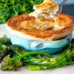 Puff pastry topped individual chicken and leek pie showing creamy filling served with broccoli.
