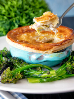 Puff pastry topped individual chicken and leek pie showing creamy filling served with broccoli.