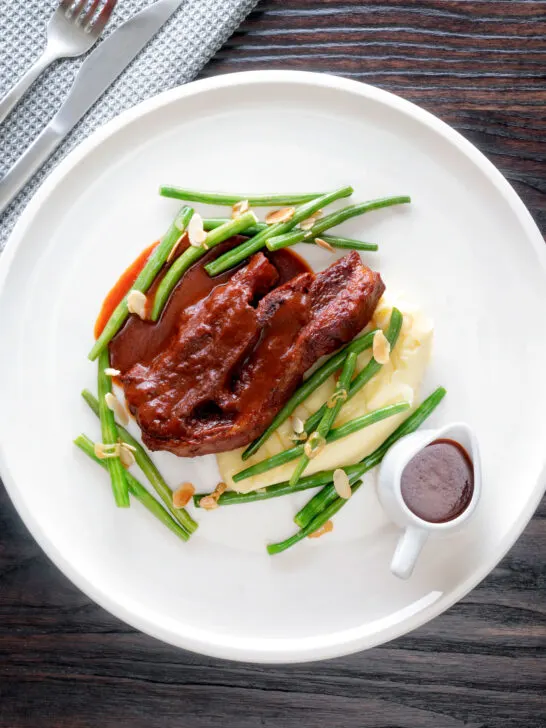 Overhead lamb shoulder chops, red wine and tomato sauce with mash and green beans.