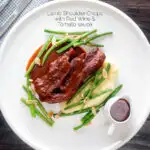 Overhead lamb shoulder chops, red wine and tomato sauce with mash and green beans featuring a title overlay.