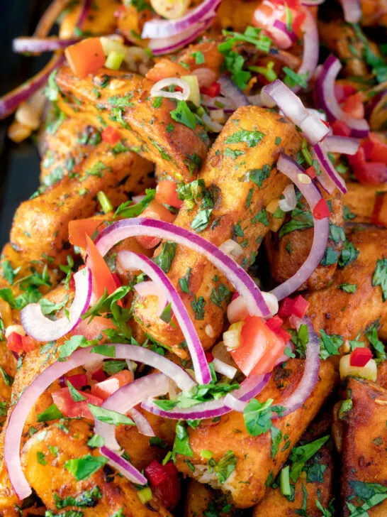 Close up masala chips or fries topped with onion, tomato, chilli and coriander.