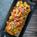 Overhead masala chips or fries topped with onion, tomato, chilli and coriander featuring a title overlay.