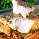Masala fish fillet (coley) cut open to show the flesh served with masala chips.