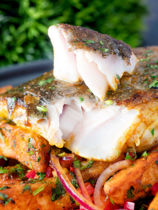 Masala fish fillet (coley) cut open to show the flesh served with masala chips.