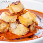 Close up garlic croutons served with homemade roasted garlic tomato soup featuring a title overlay.