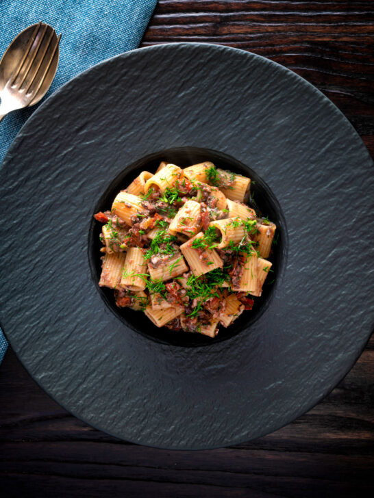 Overhead canned sardine pasta Bolognese with mezzi rigatoni and fresh dill.