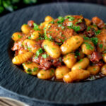 Steaming hot portion of sausage gnocchi in a tomato sauce featuring a title overlay.