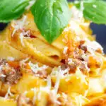Close up slow cooker bolognese sauce served with tagliatelle pasta and fresh basil featuring a title overlay.