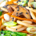 Close up Vegan yaki udon noodles with shiitake mushrooms, carrots and pak choi.