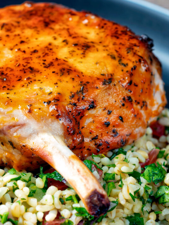 Clos up rose harissa glazed roasted pork chops with bulgur wheat salad.