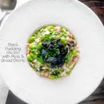 Overhead black pudding risotto with bacon, broad beans and garden peas featuring a title overlay.
