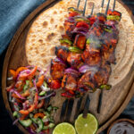 Overhead chicken shashlik kebab sticks with chapatis and kachumber salad.
