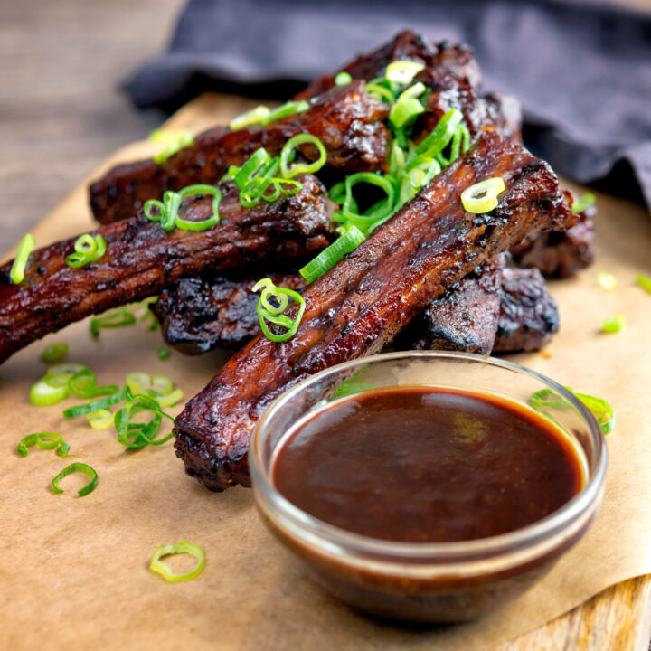 Chinese takeaway style spare ribs with a dipping sauce and sliced spring onions.